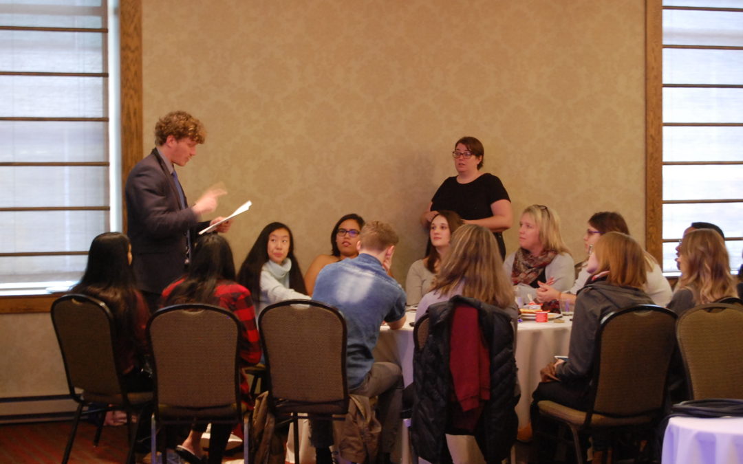 An intern speaking to a group of youth seated at a table. Un stagiaire parle à un groupe de jeunes assis à une table.